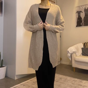 Beige lång stickad kofta - Lång, öppen beige kofta med avslappnad passform. Stickad och, perfekt att slänga över en outfit för extra lager. Koftan har lång ärm och enkel design utan knappar eller fickor. Snygg och enkel att matcha. Jag är 158 cm lång. 