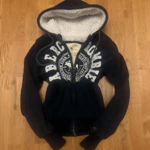 Vintage Marinblå hoodie Abercrombie & Fitch - Mysig marinblå hoodie från Abercrombie & Fitch med vit teddyfoder i huvan och stora broderade bokstäver framtill. Tröjan har två dragkedjor, Perfekt för kyliga dagar🔵|                                   Storlek: L men passar mer som S/M                         Skriv vid funderingar                                         Priset kan självklart diskuteras!