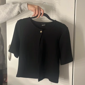 Svart kortärmad kofta - Svart kortärmad kofta från Gina Tricot med en guldig knapp som snygg detalj. Oanvänd utan lapp💕🤗