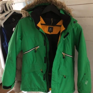Grön vinterjacka från North Bend - Snygg grön vinterjacka från North Bend med huva och fejkpäls. Jackan har flera dragkedjor, svarta och gula detaljer samt innerfoder i svart och gult. Perfekt för kalla dagar med sin varma och funktionella design. Flera praktiska fickor och justerbar huva.