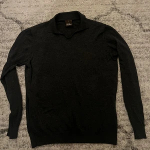 Svart polotröja från Oscar Jacobson - Stilren svart polotröja från Oscar Jacobson i storlek M. Tröjan har en klassisk krage och är långärmad, perfekt för dig som gillar en clean och enkel look. Materialet är mjukt och känns skönt mot huden, passar dig som vill ha något snyggt och bekvämt.