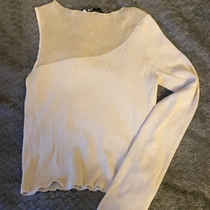 Beige enärmad topp  - Säljer en beige långärmad topp, med asymmetrisk meshdetalj upptill. Toppen har en ribbad struktur och är figurnära med en cool, modern design. Perfekt till fester!