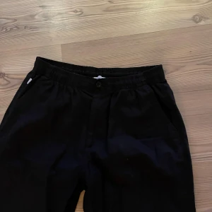 Svarta linnebyxor med rak passform - Svarta linnebyxor med elastisk midja och knappstängning. Byxorna har raka ben och sidofickor, vilket ger en chill och enkel look. Perfekta för dig som gillar stilrena och bekväma plagg i lätt material.