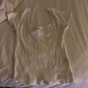 Vit ribbad kortärmad topp från Gina Tricot - Säljer en vit ribbad topp från Gina Tricot med korta ärmar och rundad halsringning. Toppen har en slim passform och är tillverkad i mjuk bomull som känns skön mot huden. Perfekt att styla med jeans eller kjol för en enkel och fräsch look.