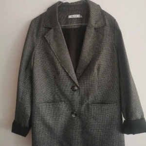 Kavaj smårutig  - En fin svart/vit/grå rutig kavaj från NA-KD Lite längre modell. Snygg både knäppt och öppen. Sparsamt använd.