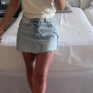 Ljusblå jeanskjol med rå kant - Säljer en ljusblå jeanskjol med klassisk femficksdesign och rå, fransig kant nedtill. Kjolen har knapp och dragkedja framtill samt en normal passform. Perfekt för dig som gillar en avslappnad och trendig stil.