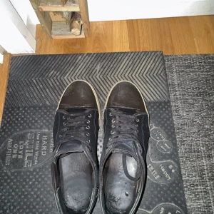 Svarta sneakers från Lanvin med mocka - Svarta sneakers från Lanvin med snygga detaljer i mocka och skinn. Skorna har rund tå, svart snörning och en kontrasterande vit sula. Tåpartiet är förstärkt med en blank svart skinnpanel som ger en cool look. Perfekt för dig som gillar stilrena och exklusiva sneakers. Skorna ser snyggare och fräschare ut i verkligheten. Kom med prisförslag! 