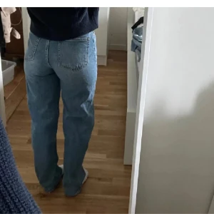 Blå raka jeans med hög midja - Säljer ett par klassiska blå jeans med hög midja och raka ben. Jeansen har fem fickor och stängs med dragkedja och knapp. Perfekta för en avslappnad och stilren look.
