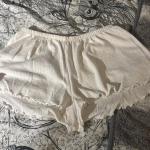 Vita ribbade shorts från 157 XS - Säljer ett par supermjuka vita shorts från 157 i storlek XS. De har ribbad struktur, elastisk midja och söt volangkant nedtill. Perfekta för chill dagar eller som pyjamasshorts. Materialet är bomull och de har en loose passform.