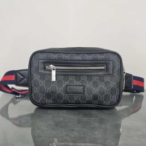 Svart axelväska från Gucci med monogram - Snygg svart axelväska från Gucci med klassiskt GG-monogram över hela väskan. Väskan har en silverfärgad dragkedja framtill och justerbart band i blått och rött. Tillverkad i slitstarkt syntetmaterial med läderdetaljer.