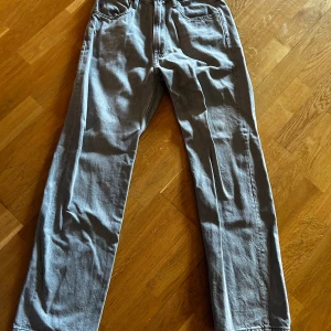 Grå jeansbyxor från G-Star RAW - Storlek 30/30. Snygga grå jeansbyxor från G-Star RAW med klassisk femficksdesign och raka ben. Byxorna har en normal passform och är tillverkade i mjukt jeanstyg. Perfekta för dig som gillar stilrena och enkla jeans med diskret logga på bakfickan.