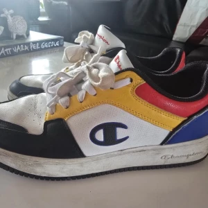 Champion sneakers i färgblock - Säljer ett par Champion sneakers med cool färgblock-design i vitt, svart, gult, rött och blått. Skorna har snörning, rund tå och platt sula. Champion-logga på sidan och tungan. Tillverkade i skinn och syntetmaterial. Perfekta för dig som gillar streetstyle och färg.