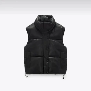Svart dunväst zara - Säljer en svart dunväst med hög krage och knappar framtill. Västen har två stora fickor på sidorna och justerbar nederkant med snörning. Materialet är glansigt och ger en cool look, perfekt att styla över en hoodie eller tröja.