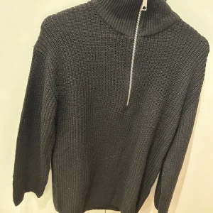 Svart stickad tröja med half zip Divided - Mysig svart stickad tröja från Divided med hög krage och snygg half zip-dragkedja. Perfekt för lager-på-lager och chill dagar. Långärmad och i grovstickat material som ger en cool vibe.