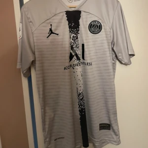 PSG Messi #30 silvergrå matchtröja - Paris Saint-Germain fotbollströja med Messi #30 på ryggen. Silvergrå med svart tryck, PSG-emblem på bröstet och Jordan-logga. Snyggt mönster i mitten och Ligue 1 Champion-märke på ärmen. Tillverkad i lätt, ventilerande material.