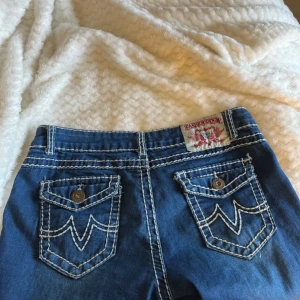 Blå jeans med kontrastsömmar - Snygga blå jeans från Fashion Denim med tydliga vita kontrastsömmar och coola fickdetaljer bak. Klassisk femficksmodell med knapp och dragkedja framtill. Jeansen har raka ben och markerade sömmar som ger en unik look.