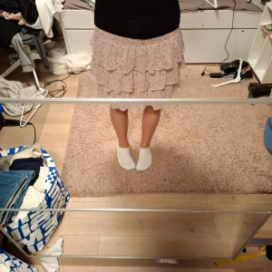 Rosa volangkjol från Lindex - Säljer en söt rosa kjol från Lindex med volanger och blommigt mönster. Kjolen har en kort längd och är gjord i mjukt bomullsmaterial. Perfekt för dig som gillar romantisk och feminin stil. Elastisk midja för skön passform. Bara använt 2 gngr