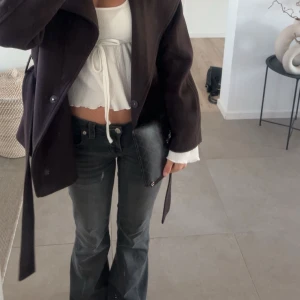 True Religion Joey - Säljer ett par svarta True Religion Joey jeans med låg midja och flare-ben. Klassiska detaljer med ficklock och silverfärgade knappar. Snygga kontrastsömmar och mjukt denimtyg som sitter riktigt bra. Perfekta för dig som gillar en retro vibe och markerad siluett. Kan gå ner i pris