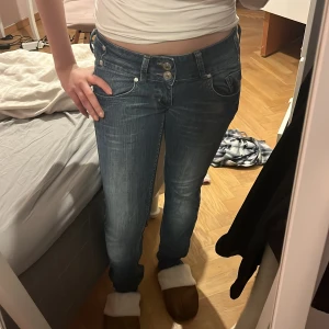 Lågmidjade Vintage jeans - Snygga blå jeans med coola dubbla knappar i midjan och unika bakfickor med extra detaljer. Jeansen har en klassisk tvättad look och raka ben. Perfekta för dig som gillar en lite annorlunda stil på dina jeans.