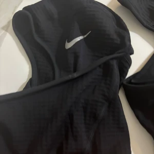 Svart bikini från Nike - Snygg svart bikini från Nike med klassisk silvrig swoosh-logga på toppen. Modellen har sportig design och är tillverkad i mjukt syntetmaterial som torkar snabbt. Perfekt för dig som gillar att hänga vid poolen eller stranden och vill ha en stilren look.