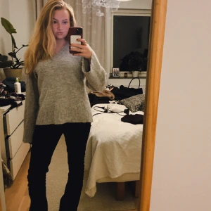 Grå stickad tröja med v-ringning - Mysig grå stickad tröja med v-ringad hals och långa ärmar. Tröjan har en avslappnad passform och ribbade muddar vid ärmslut och nederkant. Perfekt för lager-på-lager och enkel att matcha med jeans eller kjol.