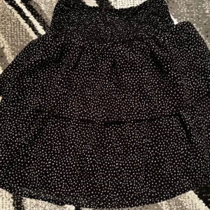 Svart prickig volangkjol XS - Supersöt svart kortkjol med vita prickar och volangdetaljer. Kjolen har smock i midjan för en bekväm passform och ett luftigt, flowy tyg som ger en lätt känsla. 