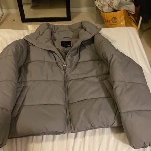 Grå pufferjacka från 157, M - Säljer en grå pufferjacka från 157 i storlek M. Jackan har en hög krage, dragkedja framtill och elastiska muddar vid ärmsluten. Materialet är polyester och jackan har en clean, oversized look som är perfekt för kalla dagar.Köpt förra året men ej använt.Snygg grå färg.