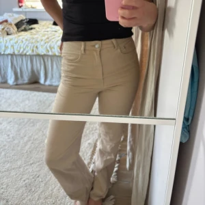 Beiga raka byxor med hög midja - Snygga beiga byxor med hög midja och raka ben. Byxorna har klassisk femficksdesign och stängs med knapp och dragkedja. Perfekta att styla med en crop top eller hoodie för en chill look.