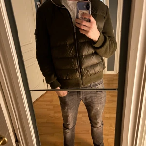 Olivgrön pufferjacka från Bvaldi - Säljer en olivgrön pufferjacka från Bvaldi i storlek L. Jackan har quiltad framsida, stickade ärmar och muddar samt dragkedja framtill. Snygg detalj med ficka och logga på ena ärmen. Perfekt för kyligare dagar. Mvh Pelle