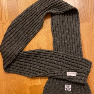 Moncler Halsduk - Fräsch halsduk från Moncler perfekt nu för kallare väder.   OBS: Märkes taggen sitter inte helt (se bild 4), men för en självsäker eller sy-kunnig person bör det inte vara något problem. Pga skadan är priset såpass lågt. Utöver taggen så är halsduken felfri och har inga tecken på användning.   Fraktas inom 24h📦 Kommer från päls- och rökfritt hem🚭  Mått: 150cm lång.   Skriv vid fler frågor 🌟
