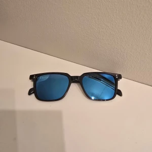 Svarta solglasögon med blå spegelglas - Snygga solglasögon med svart båge och blå spegelglas. Klassisk fyrkantig form som passar de flesta ansikten. Perfekta för att ge din stil en cool touch i sommar.
