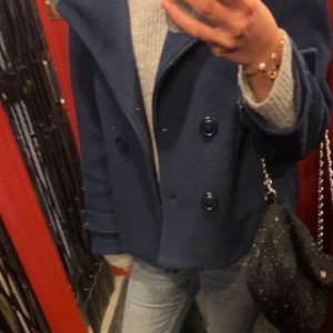 Mörkblå kappa från design by si  - Snygg marinblå kappa från design by si. Köpte för två år sedan och har blivit använd. Två knappar saknas även och den är lite nopprig men kan tas bort, därpå det billiga priset! Storlek xs/s