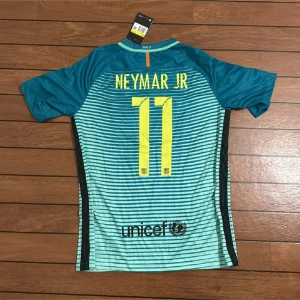 Barcelona Neymar Jr fotbollströja S - Snygg Barcelona fotbollströja med Neymar Jr och nummer 11 på ryggen. Tröjan är kortärmad, har blå och turkosa ränder, officiella Champions League-patchar på ärmarna och Qatar Airways som sponsor. Tillverkad i lätt Dri-FIT material som andas.