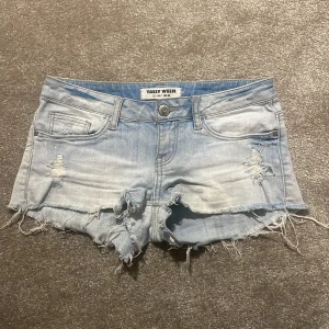 Ljusblå jeansshorts Tally Weijl - Säljer ett par ljusblå lågmidjade jeansshorts från Tally Weijl med slitna detaljer och fransig kant. Shortsen har klassisk femficksdesign, låg midja och är tillverkade i bomull. Perfekta för sommaren och ger en cool, avslappnad vibe.