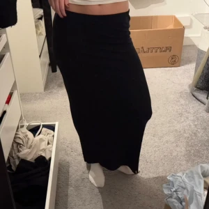 Svart långkjol i mjukt material - Säljer en svart långkjol med rak och tight passform. Kjolen är enkel och stilren utan mönster eller detaljer, och är gjord i ett mjukt och stretchigt material som sitter skönt mot kroppen. Perfekt att matcha med crop tops eller hoodies.