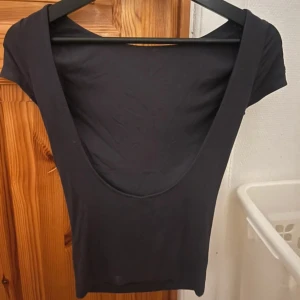 Tröja med öppen rygg - Säljer en mörkgrå topp med med öppen rygg. Toppens stil är enkel och tight, perfekt för att matcha med höga jeans eller kjol. Materialet känns mjukt och stretchigt.