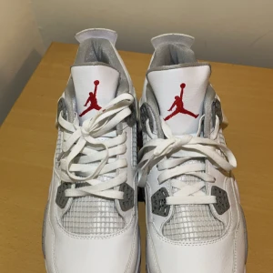 Nike Air Jordans i vitt och grått - Snygga Nike Air Jordans i vitt med grå detaljer och röd logga. Skorna har snörning och en klassisk design med meshpaneler för extra stil och ventilation. Perfekta för dig som vill ha en ikonisk look.