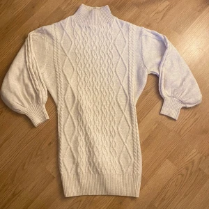 Stickad klänning från H&M - Säljer en mysig vit stickad klänninh från H&M med ett snyggt flätmönster. Tröjan har långa ärmar och en hög krage. Perfekt för kyliga dagar! Den är oversize och skulle säga att den passar xs-m