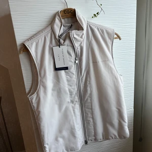 Vit väst från Tiger of Sweden - Snygg väst från Tiger of Sweden med dragkedja framtill. Perfekt för lager-på-lager under kyligare dagar. Stilren design med hög krage. Vatten- och vindavvisande  i polyestertwill. Fickor i sidosömmarna. Lättfodrad. Regular fit.  Helt ny med prislapp. Aldrig använd.  Rök- och djurfritt hem 🐅 