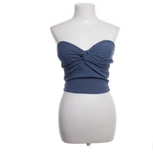 Blå tubtopp - Säljet en blå tubtopp med en twistad detalj framtill. Toppen är axelbandslös och har en tight passform. Den har endast använts några gånger och har inga tecken på användning.