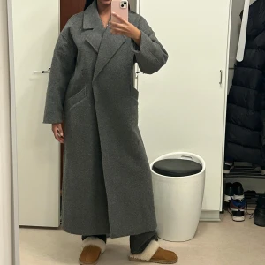 Grå lång kappa - Säljer en grå lång kappa, den är i bra skick men lite nopprig på armarna!