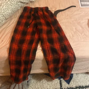 Röd och svart rutig byxa med snörning - Säljer ett par bekväma byxor i röd och svart rutig design. Byxorna har en elastisk midja med snörning för justerbar passform. Perfekta för en avslappnad stil. Helt nya jag skulle säga de är M elr L men jag köpte de i XS men de var alldeles för stora funkade inte alls på mig. Går att diskutera pris