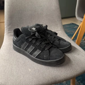 Adidas Campus 00s - Snygga svarta sneakers från Adidas i mocka, skorna är knappast använda och har bara legat hemma och samlat damm så bestämmer mig för att sälja de!🔥 Extra snören medföljes (vita), boxen ingår INTE. Har ni fler frågor är det bara att skicka ett PM!   Priset är inte hugget i sten!💰                                                                                           Mvh