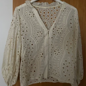 Benvit blus med mönstrade hål - En fin blus med mönstrade hål. Man er igenom hålen men det blir väldigt snyggt tycker jag, särskilt på sommaren. Den är benvit och har ballongliknande ärmar! 