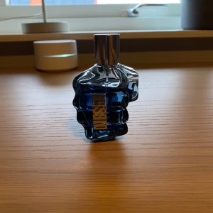 Blå parfymflaska från Diesel - Säljer en cool blå parfymflaska från Diesel, formad som en knytnäve. Flaskan har en metallisk kork och en unik design som verkligen sticker ut. En manlig doft som är lätt att gilla. Inte använd särskilt mycket.