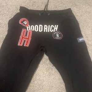 Svarta mjukisbyxor från Hoodrich - Snygga svarta mjukisbyxor från Hoodrich med tryck och broderade detaljer. Byxorna har snörning i midjan och är perfekta för en avslappnad stil. De har en cool design med logotypdetaljer på framsidan. Storlek L passar 170