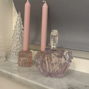 Parfym från Ariana Grande - Elegant parfymflaska i ljuslila glas med en unik kristallformad design. Flaskan har en avtagbar del som ger en lyxig känsla. Perfekt för den som älskar en stilren och modern look på sin parfymhylla.