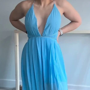Bal-/festklänning  - Snygg blå långklänning med djup v-ringad urringning och halterneck-design. Klänningen har en slits och elastiska band som kan knytas på flertalet olika sätt! Använd 1 gång på bal i strl S