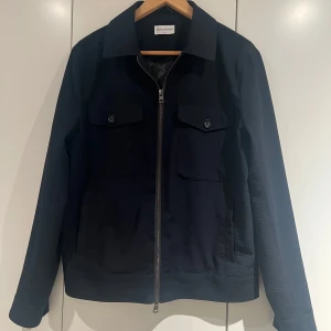 Mörkblå jacka från These Glory Days - Snygg mörkblå jacka från These Glory Days med dragkedja och knappar. Jackan har en stilren design med två bröstfickor och långa ärmar. Perfekt för en stilren look. Nypris runt 2.5k. Jackan har inga defekter, men kan va dammig på nåt ställe. Fraktar oftast inom 24h. 