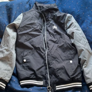 Svart och grå bomberjacka från Warp - Säljer en snygg svart och grå bomberjacka från Warp. Jackan har en dragkedja framtill och två fickor med knappar. Ärmarna är gråa och kroppen är svart med vita detaljer. Perfekt för en cool och avslappnad stil. Den är i storlek 158 och är perfekt till våren eller hösten💕